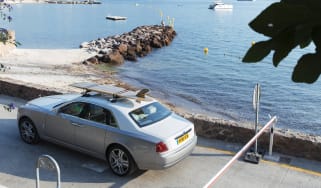 Rolls-Royce Ghost with surfboard on roof next to shoreline