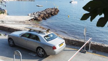 Rolls-Royce Ghost with surfboard on roof next to shoreline